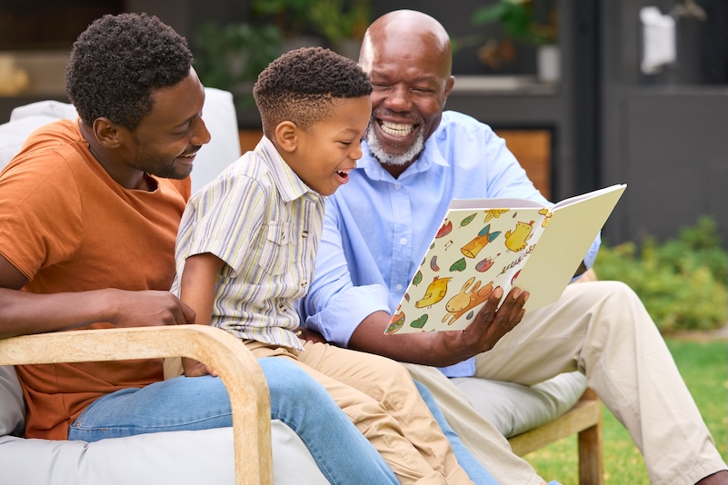 Grandfather, son, and grandson enjoying a book together — three generations CareBridge serves
